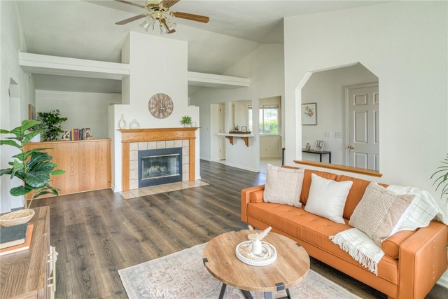 living area with arched walkways, lofted ceiling, wood finished floors, ceiling fan, and a tile fireplace