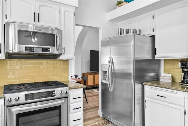 kitchen with dark stone counters, stainless steel appliances, backsplash, white cabinetry, and arched walkways
