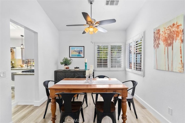 dining room featuring light wood-style floors, a ceiling fan, visible vents, and baseboards
