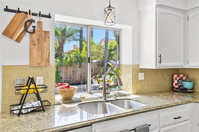 kitchen with tasteful backsplash, light stone countertops, a sink, white cabinetry, and pendant lighting