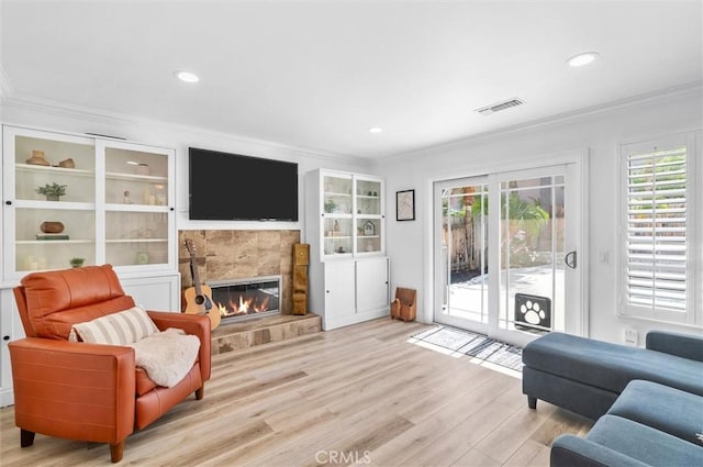 living room with visible vents, a tiled fireplace, light wood-type flooring, and ornamental molding