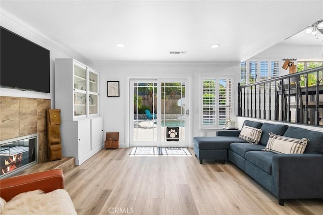 living room featuring visible vents, a healthy amount of sunlight, ornamental molding, a fireplace, and wood finished floors