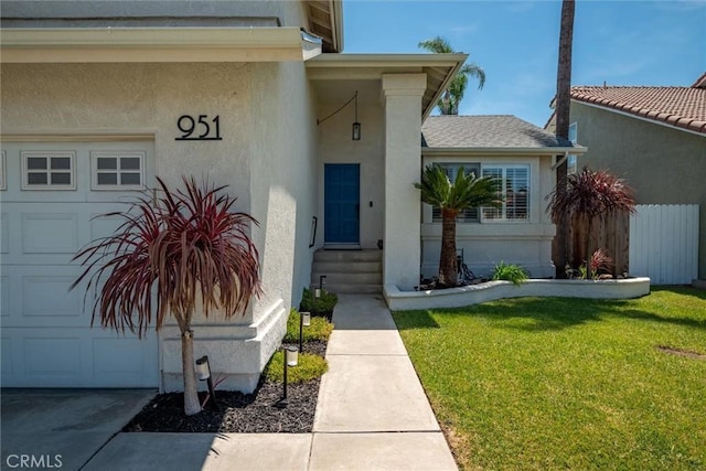 entrance to property with an attached garage, driveway, a yard, and stucco siding