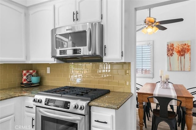 kitchen with dark stone countertops, appliances with stainless steel finishes, white cabinets, backsplash, and a ceiling fan