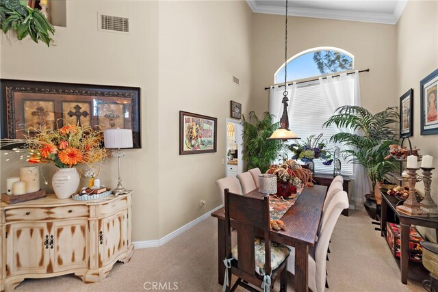 carpeted dining room with visible vents, baseboards, a high ceiling, and ornamental molding