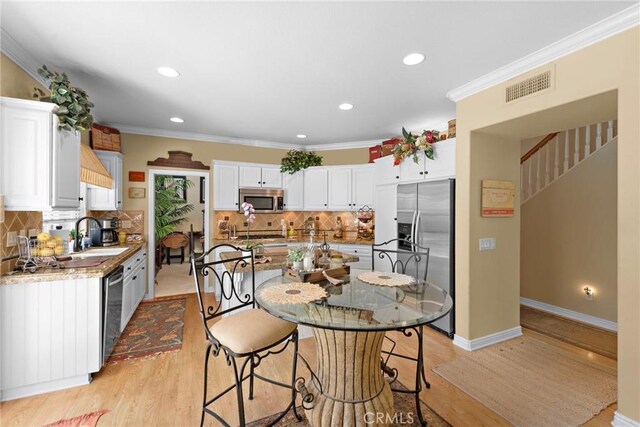 kitchen featuring light wood-style flooring, a sink, appliances with stainless steel finishes, visible vents, and backsplash