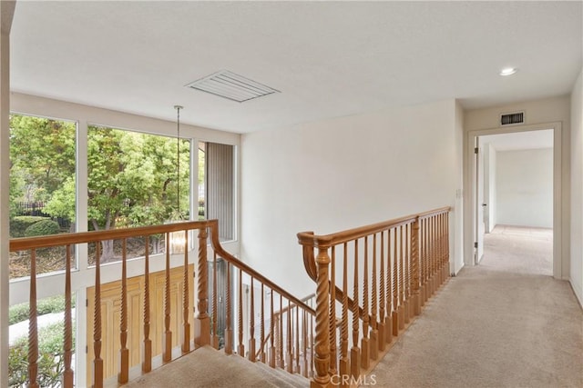 hall with visible vents, a wealth of natural light, light carpet, and an upstairs landing