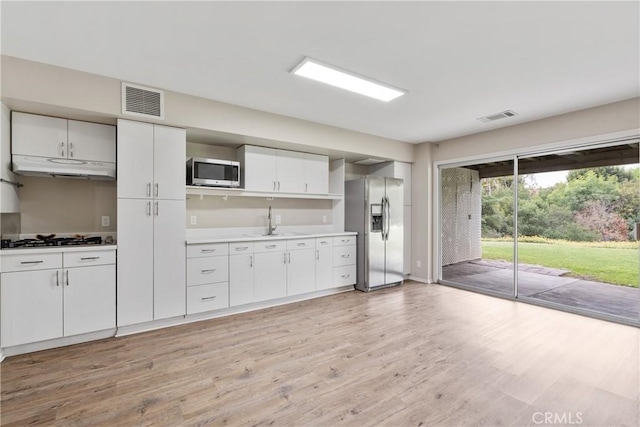 kitchen featuring under cabinet range hood, light wood-type flooring, visible vents, and stainless steel appliances