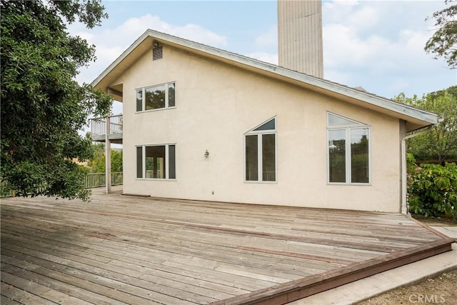 rear view of property featuring a wooden deck, a chimney, a balcony, and stucco siding