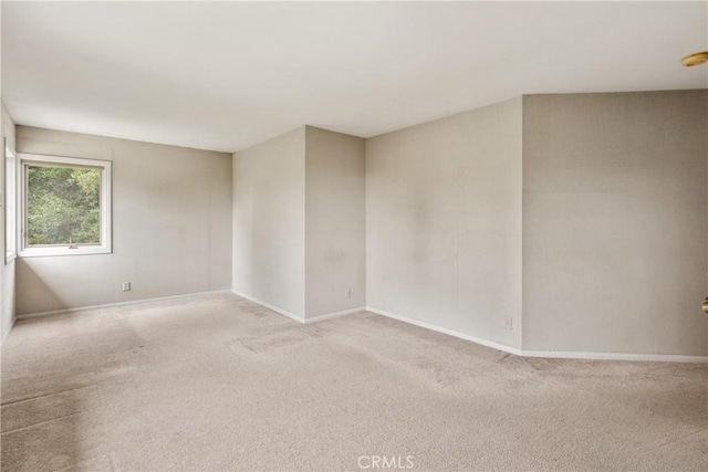 spare room featuring light carpet and baseboards