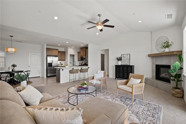 living room featuring light carpet, visible vents, a ceiling fan, a tile fireplace, and vaulted ceiling