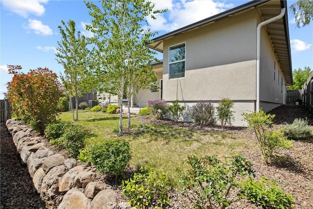 view of side of home featuring a lawn, fence, and stucco siding