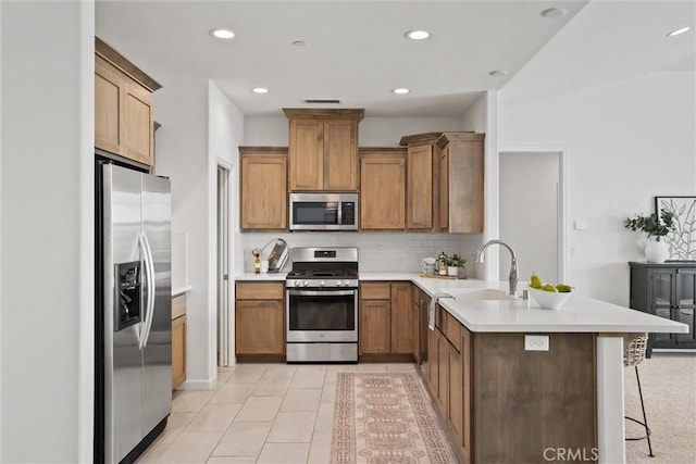 kitchen featuring decorative backsplash, a peninsula, a kitchen bar, a sink, and appliances with stainless steel finishes
