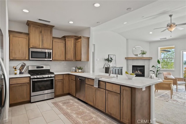 kitchen with a peninsula, open floor plan, a tile fireplace, a sink, and stainless steel appliances