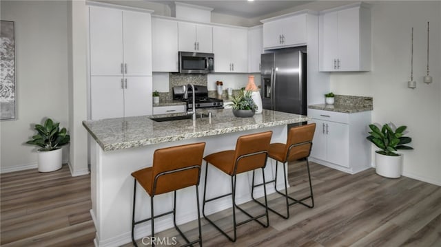 kitchen with tasteful backsplash, a breakfast bar area, appliances with stainless steel finishes, white cabinetry, and dark wood-style flooring
