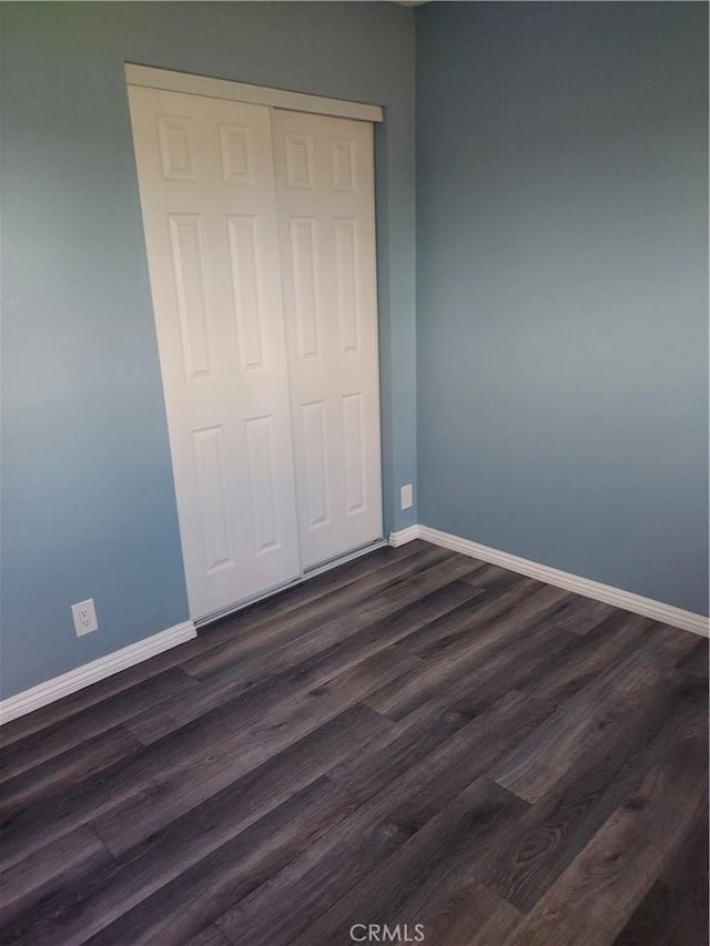 unfurnished bedroom with baseboards, dark wood-type flooring, and a closet