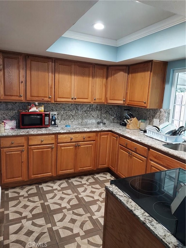 kitchen featuring brown cabinets, stove, a tray ceiling, a sink, and crown molding