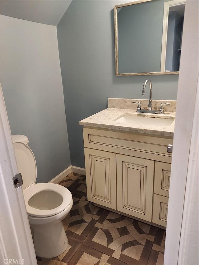 half bathroom with vanity, toilet, and baseboards