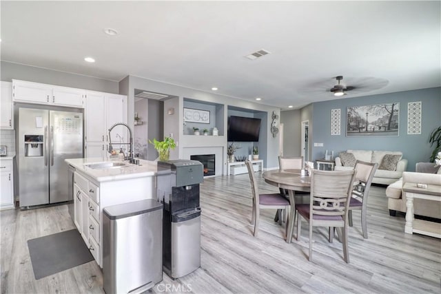 kitchen with stainless steel fridge, a sink, light wood-style floors, a glass covered fireplace, and open floor plan