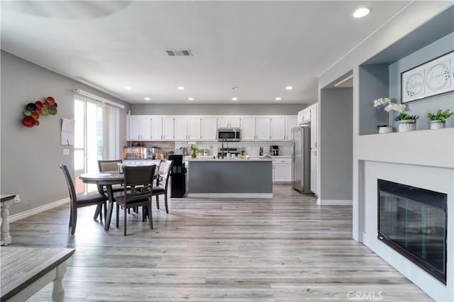 dining space featuring a glass covered fireplace, recessed lighting, baseboards, light wood-type flooring, and visible vents