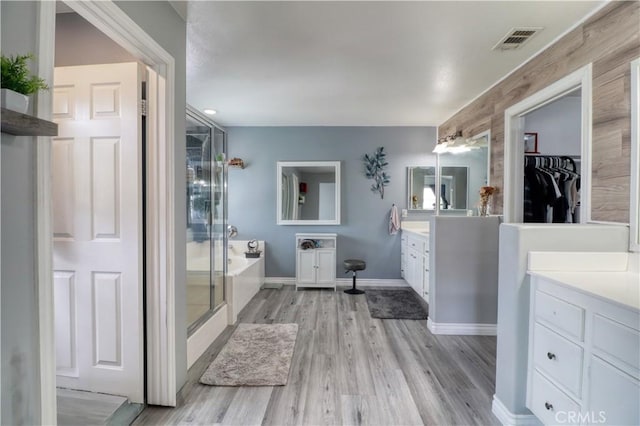full bathroom featuring two vanities, a shower stall, wood finished floors, visible vents, and a bath