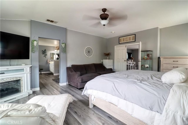 bedroom featuring visible vents, wood finished floors, a fireplace, baseboards, and a ceiling fan