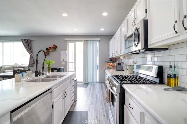 kitchen with a sink, appliances with stainless steel finishes, white cabinets, and a healthy amount of sunlight