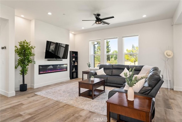living area with a ceiling fan, baseboards, and light wood-style floors