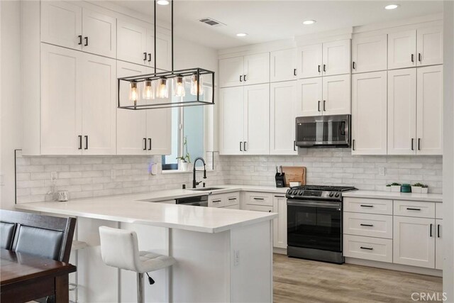 kitchen featuring stainless steel microwave, a sink, a peninsula, white cabinetry, and gas range