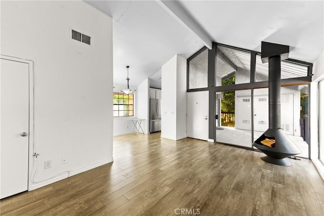 unfurnished living room featuring beam ceiling, a wood stove, high vaulted ceiling, wood finished floors, and baseboards