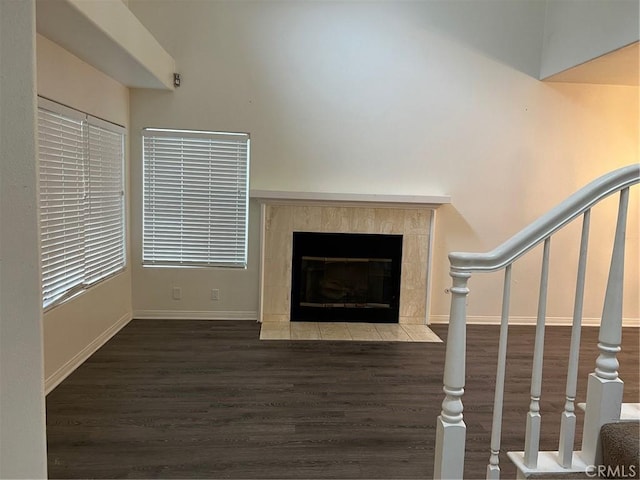 unfurnished living room featuring baseboards, wood finished floors, a tiled fireplace, and stairs