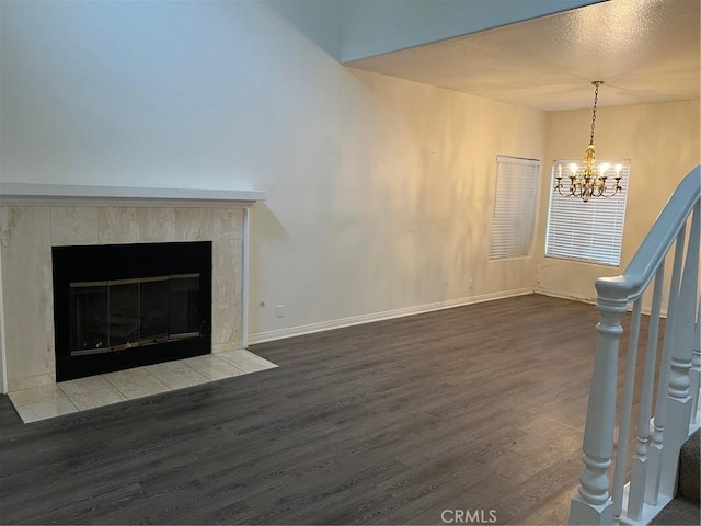 unfurnished living room featuring baseboards, a tile fireplace, wood finished floors, and a chandelier