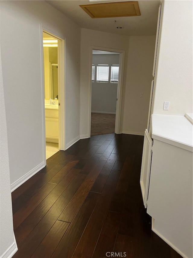 hallway featuring attic access, baseboards, dark wood-style flooring, and a sink