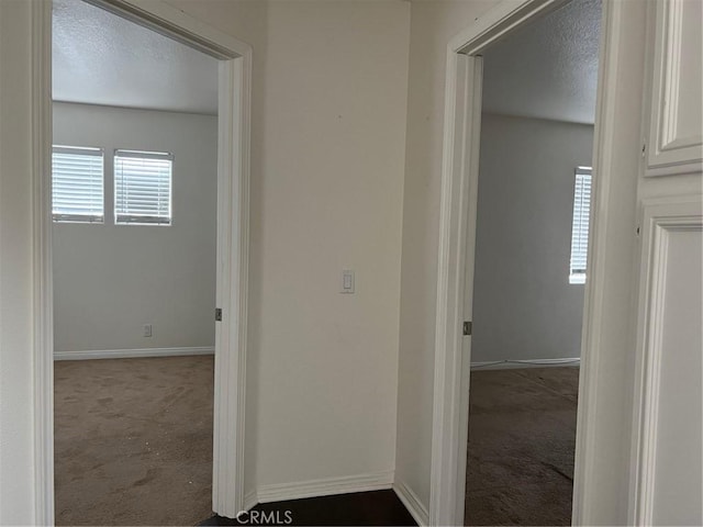 hall with baseboards, dark colored carpet, and a textured ceiling