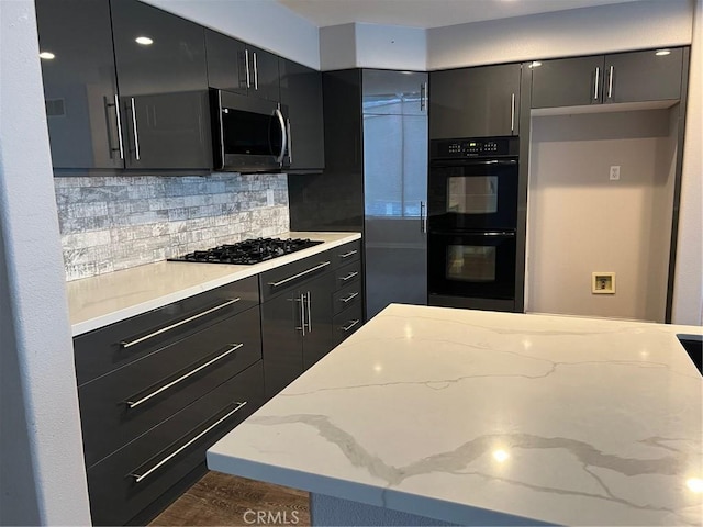 kitchen with dark cabinets, modern cabinets, light stone countertops, decorative backsplash, and black appliances
