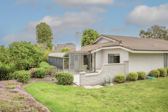 back of property with a tile roof, a sunroom, a yard, a chimney, and stucco siding