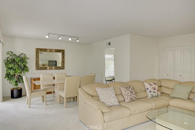 living area featuring a textured ceiling, visible vents, rail lighting, and light carpet