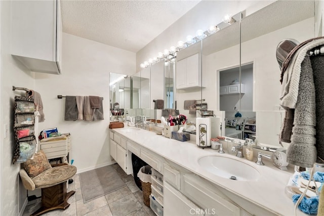 bathroom featuring a textured ceiling, a sink, double vanity, and baseboards