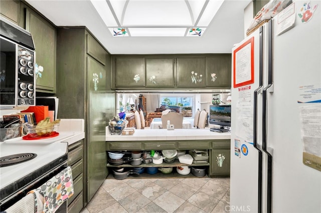 kitchen featuring green cabinetry, black microwave, freestanding refrigerator, and range with electric stovetop
