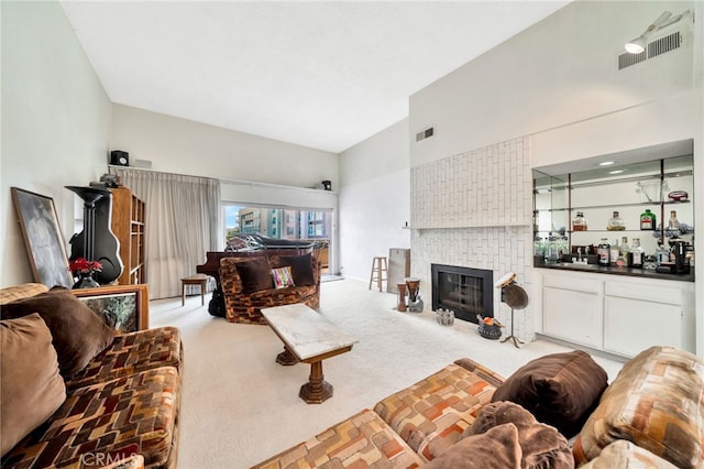 living area featuring visible vents, high vaulted ceiling, carpet flooring, and a brick fireplace