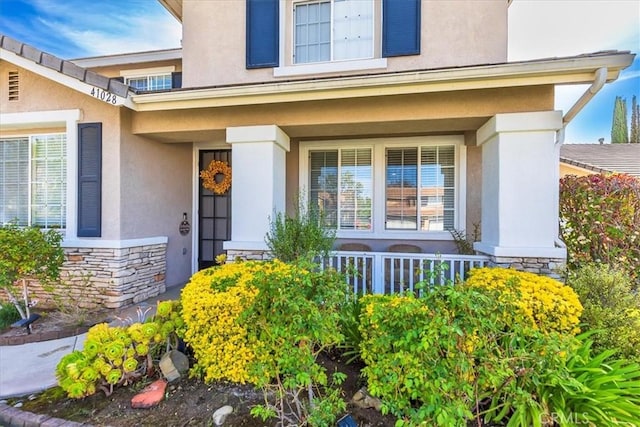 view of exterior entry with a porch, stucco siding, and stone siding