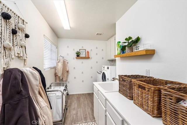 clothes washing area with visible vents, separate washer and dryer, a sink, cabinet space, and light wood finished floors