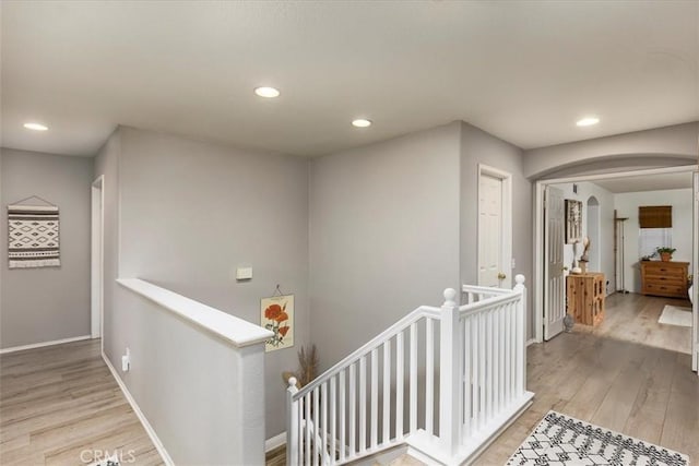hallway featuring light wood-style floors, recessed lighting, arched walkways, and an upstairs landing