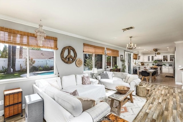 living area featuring an inviting chandelier, light wood-style flooring, crown molding, and visible vents