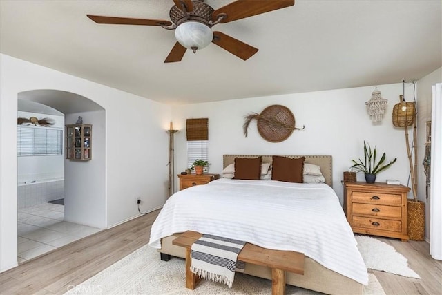 bedroom featuring arched walkways, ceiling fan, ensuite bathroom, and light wood finished floors