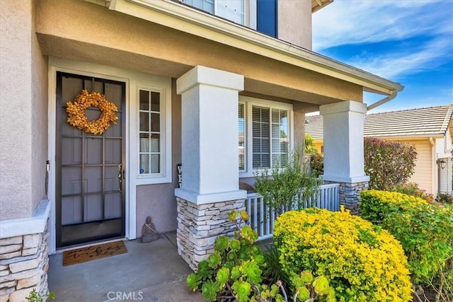 entrance to property featuring stucco siding, a porch, and stone siding