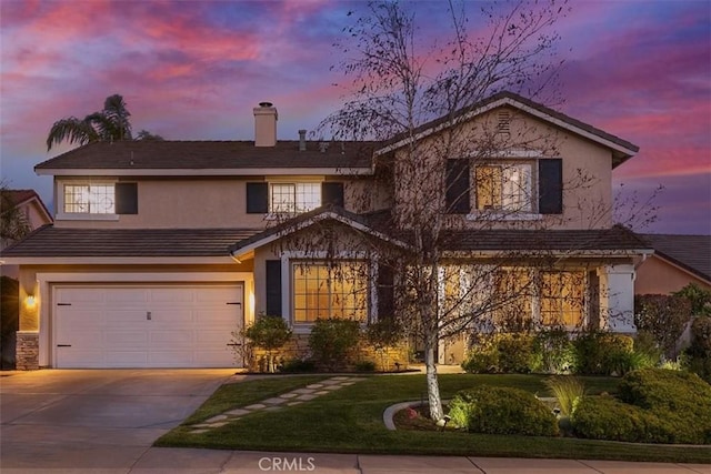 traditional-style house featuring a chimney, a yard, an attached garage, concrete driveway, and stucco siding
