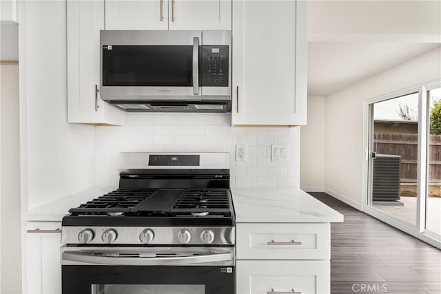 kitchen featuring white cabinets, stainless steel appliances, backsplash, wood finished floors, and light stone countertops