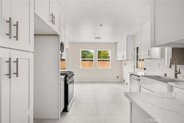 kitchen featuring stainless steel appliances, a sink, white cabinetry, marble finish floor, and light stone counters