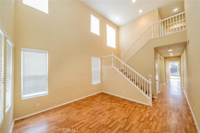 3882 Strand Way, Perris, CA 92571 - unfurnished living room with a high ceiling, light wood-style flooring, stairs, plenty of natural light, and baseboards